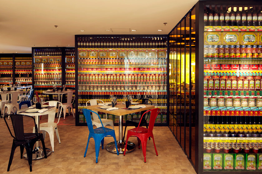zona restaurante mesa para cuatro sillas thonet rojas azules blancas y negras estanterias retroiluminadas con productos tradicionales españoles