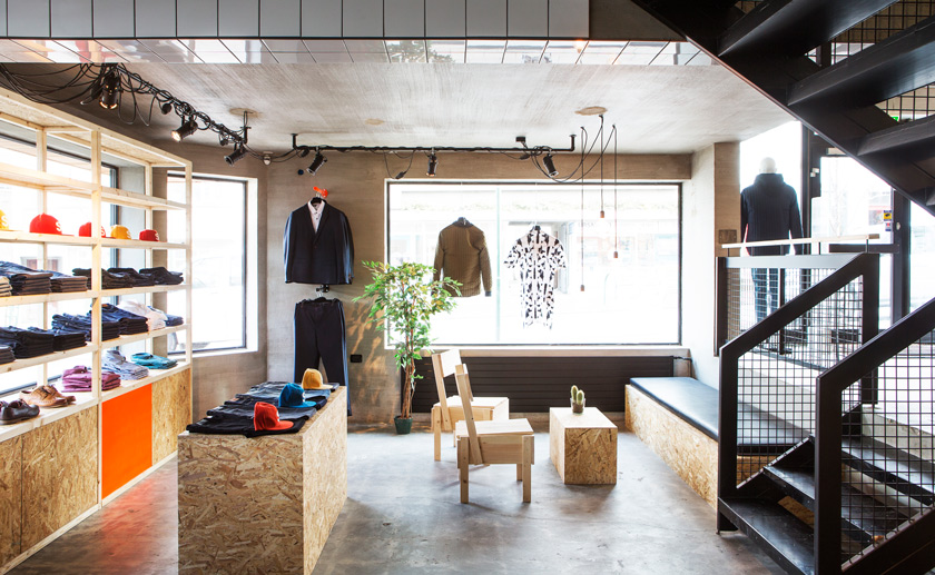 HAFstudio Suit store entrada escalera acero y pavimento de hormigón alisado con mobiliario de madera laminada 