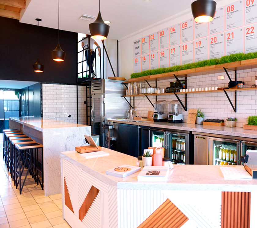 barra de cafetería menú en la pared taburetes nevera industrial zumos postres estanterías hierba falsa baldosas blancas 