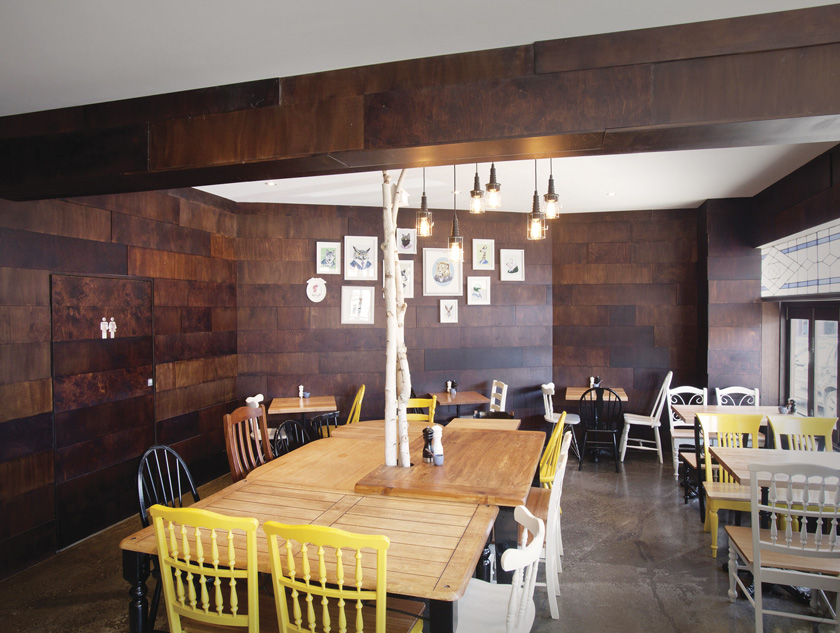 pared recubierta de láminas de madera oscura acogedor suelo de cemento alisado sillas amarillas negras y blancas