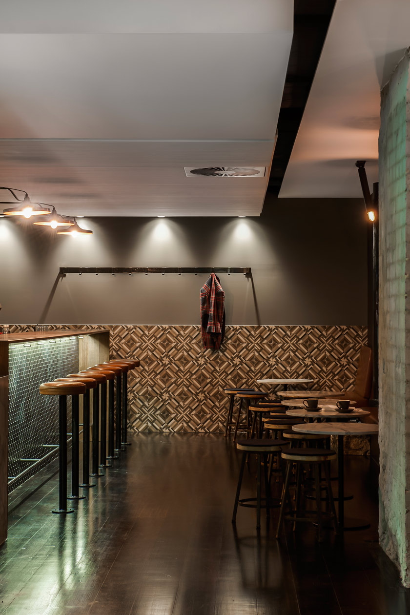 barra del restaurante con taburetes y alicatado de baldosas marrones en pared mesas bajas de madera con asientos 