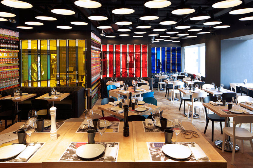 mesas restaurante con vajilla paneles separadores de colores hacen de fachada sofa negro chesterfiel ventanales luz natural